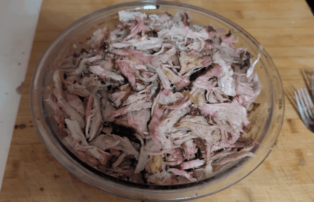 Fresh smoked pulled pork in glass bowl on cutting board. 